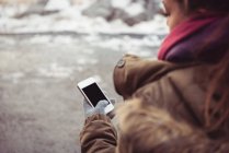 Крупный план женщины с мобильного телефона на берегу реки зимой — стоковое фото