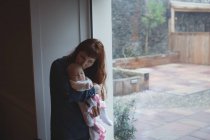 Mère embrasser bébé sur la tête par la fenêtre — Photo de stock