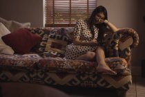 Donna che utilizza il telefono cellulare sul divano in soggiorno a casa — Foto stock