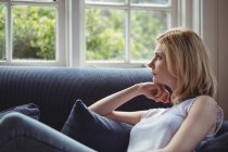 Thoughtful woman sitting on sofa in living room at home — Stock Photo
