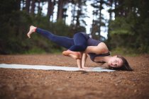 Жінка виконує йогу на тренувальному килимку в лісі — стокове фото