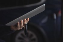 Mann hält Autoschlüssel und digitales Tablet in Garage, Nahaufnahme — Stockfoto