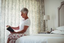 Seniorin liest Buch zu Hause im Schlafzimmer — Stockfoto