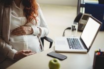Partie médiane de la femme d'affaires enceinte tenant ventre au bureau — Photo de stock