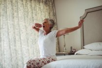 Senior woman yawning on bed in bedroom at home — Stock Photo