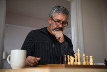Внимательный человек играет в шахматы дома — стоковое фото