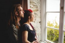 Молодая пара хипстеров, стоящая у окна дома — стоковое фото