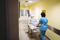 Visión borrosa del médico y la enfermera empujando a un paciente mayor en camilla en el pasillo del hospital - foto de stock