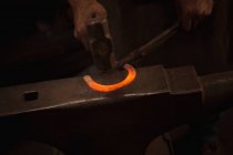 Mãos de ferreiro trabalhando em uma peça de metal com martelo na oficina — Fotografia de Stock