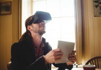 Hipster holding digital tablet while using virtual reality simulator at home — Stock Photo