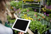 Imagen recortada de Floristería femenina utilizando tableta digital en el centro del jardín - foto de stock