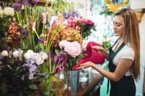 Fleuriste femelle versant de l'eau dans un vase à fleurs à sa boutique de fleurs — Photo de stock