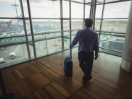 Vista traseira do homem de negócios com bagagem olhando através da janela de vidro no aeroporto — Fotografia de Stock