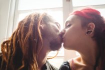 Joven pareja hipster besándose contra ventana en casa - foto de stock