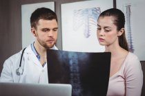 Fisioterapeuta explicando radiografía de columna vertebral a paciente femenina en clínica - foto de stock