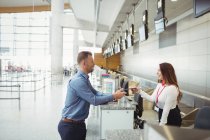 Asistente de facturación de la aerolínea entrega de pasaporte al pasajero en el mostrador de facturación del aeropuerto - foto de stock