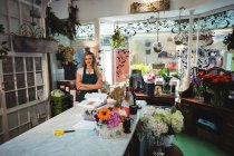 Жіночий флорист стоїть з гербами, схрещеними у квітковому магазині — стокове фото