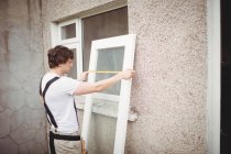Плотник измеряет дверь снаружи дома — стоковое фото
