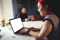 Хипстер женщина с помощью ноутбука в то время как мужчина сидит в фоновом режиме дома — стоковое фото