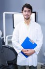 Portrait of smiling dentist standing with a clipboard at dental clinic — Stock Photo