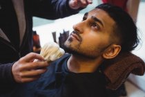 Mann rasiert sich Bart im Friseurladen mit Rasierpinsel — Stockfoto