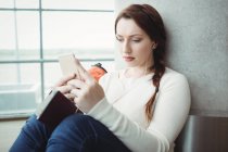 Жінка слухає музику на мобільному телефоні, сидячи в зоні очікування — стокове фото
