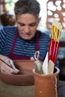 Close-up of paintbrush and work tool in pot with potter working on background — Stock Photo