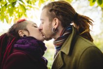 Крупним планом пара хіпстерів цілується, стоячи в парку — стокове фото