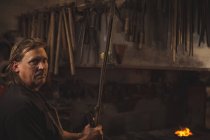 Schmied hält Eisenstange in Werkstatt — Stockfoto