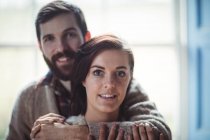 Mann umarmt Frau zu Hause und blickt in Kamera — Stockfoto
