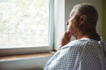 Старший чоловік у вдумливому настрої дивиться через вікно в лікарні — стокове фото