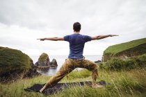 Rear view of man performing stretching exercise on cliff — Stock Photo