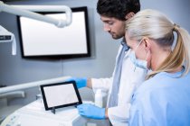 Стоматолог и зубной ассистент, работающий над цифровым планшетом в стоматологической клинике — стоковое фото