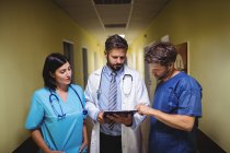 Doctor interacting over report with ward boy and nurse in hospital corridor — Stock Photo