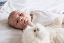 Adorable baby lying on bed with teddy bear at home — Stock Photo