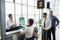 Mujer dando su pasaporte a la azafata de check-in de la aerolínea en el mostrador de check-in del aeropuerto - foto de stock