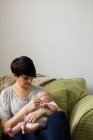 Mutter füttert ihr Baby zu Hause im Wohnzimmer — Stockfoto