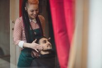 Мужчина получает массаж лица от парикмахера в парикмахерской — стоковое фото