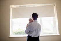 Rear view of mother standing near window and holding her sleeping baby — Stock Photo