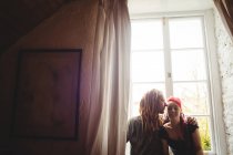 Jovem casal hipster abraçando contra a janela em casa — Fotografia de Stock