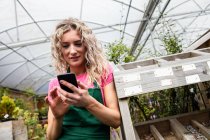 Female florist using mobile phone in garden centre — Stock Photo