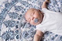 Ребенок спит с манекеном во рту на кровати дома — стоковое фото