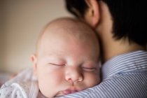 Primer plano del bebé durmiendo en el hombro de la madre en casa - foto de stock