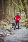 Vue de face du motard tenant un vélo tout en marchant dans le ruisseau à la forêt — Photo de stock