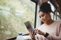 Mujer joven usando tableta digital mientras está sentado en el tren - foto de stock