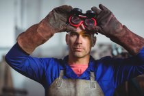 Male welder holding welding goggles in workshop — Stock Photo
