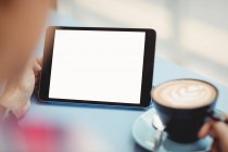 Imagen recortada de la persona sosteniendo la tableta mientras toma café en el restaurante - foto de stock