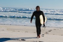 Серфер, гуляющий по пляжу в солнечный день — стоковое фото