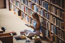 Frau sitzt und liest Buch in Bibliothek — Stockfoto