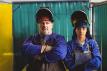 Portrait of male and female welder standing with arms crossed in workshop — Stock Photo